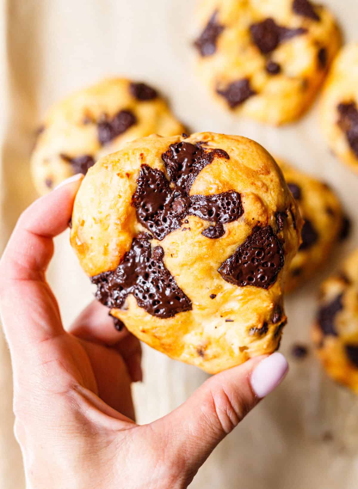 Hand holding a golden cottage cheese scone topped with pools of melted dark chocolate