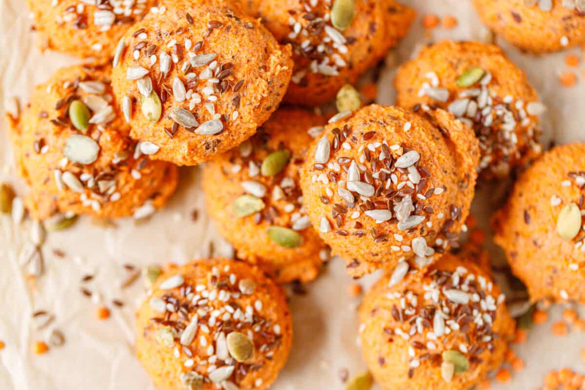 Red lentil bread rolls topped with sesame, flax, and pumpkin seeds, stacked on parchment paper