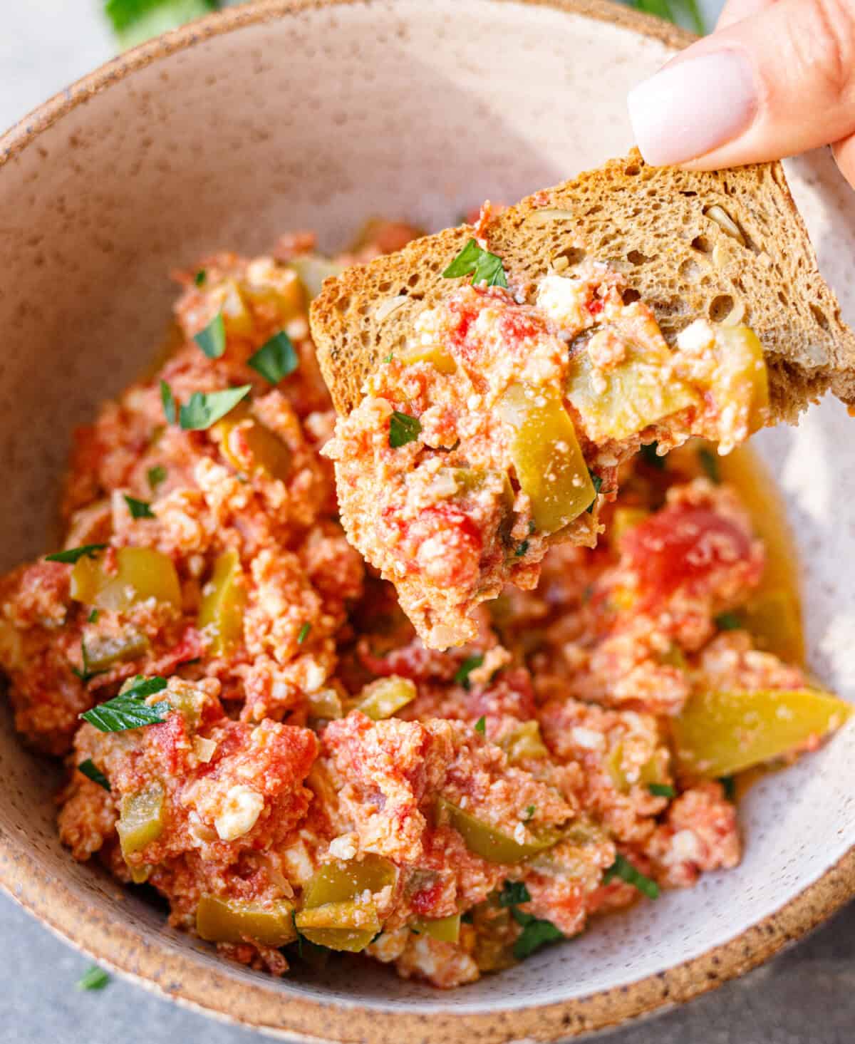 Hand dipping a piece of toasted bread into a bowl of Bulgarian mish mash