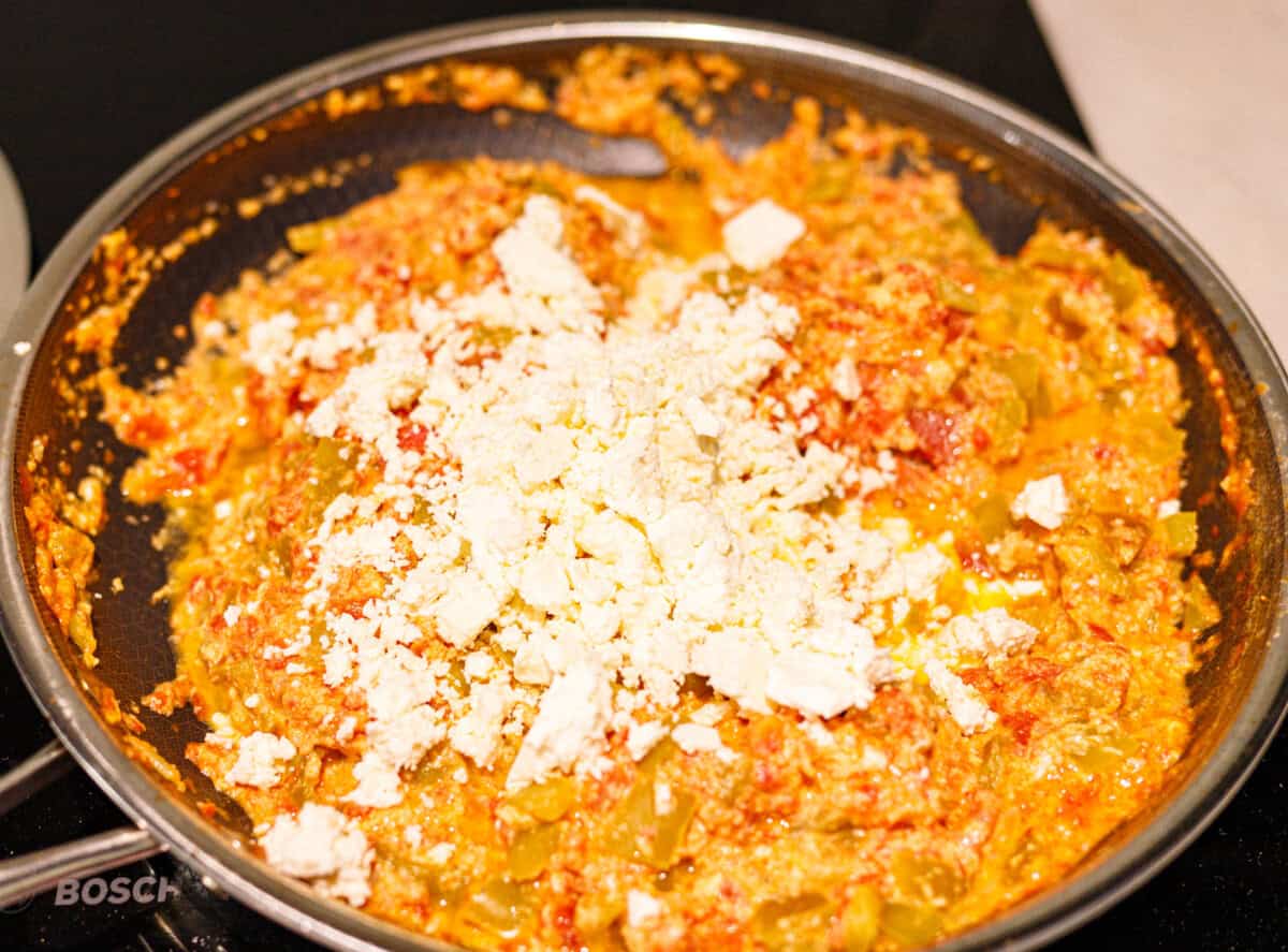 Crumbled feta scattered over cooked mish mash in a skillet