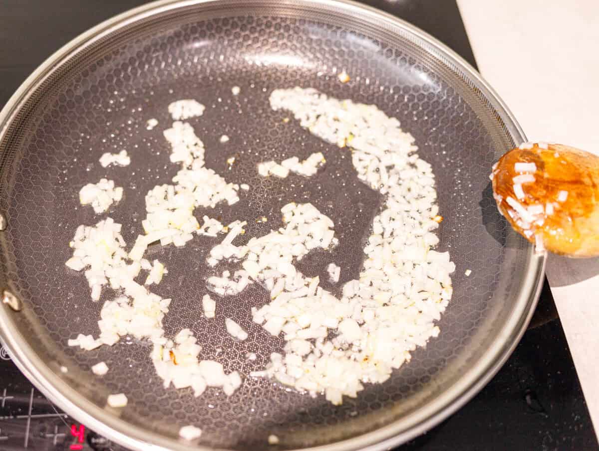 Diced onion cooking in oil in a skillet with a wooden spoon