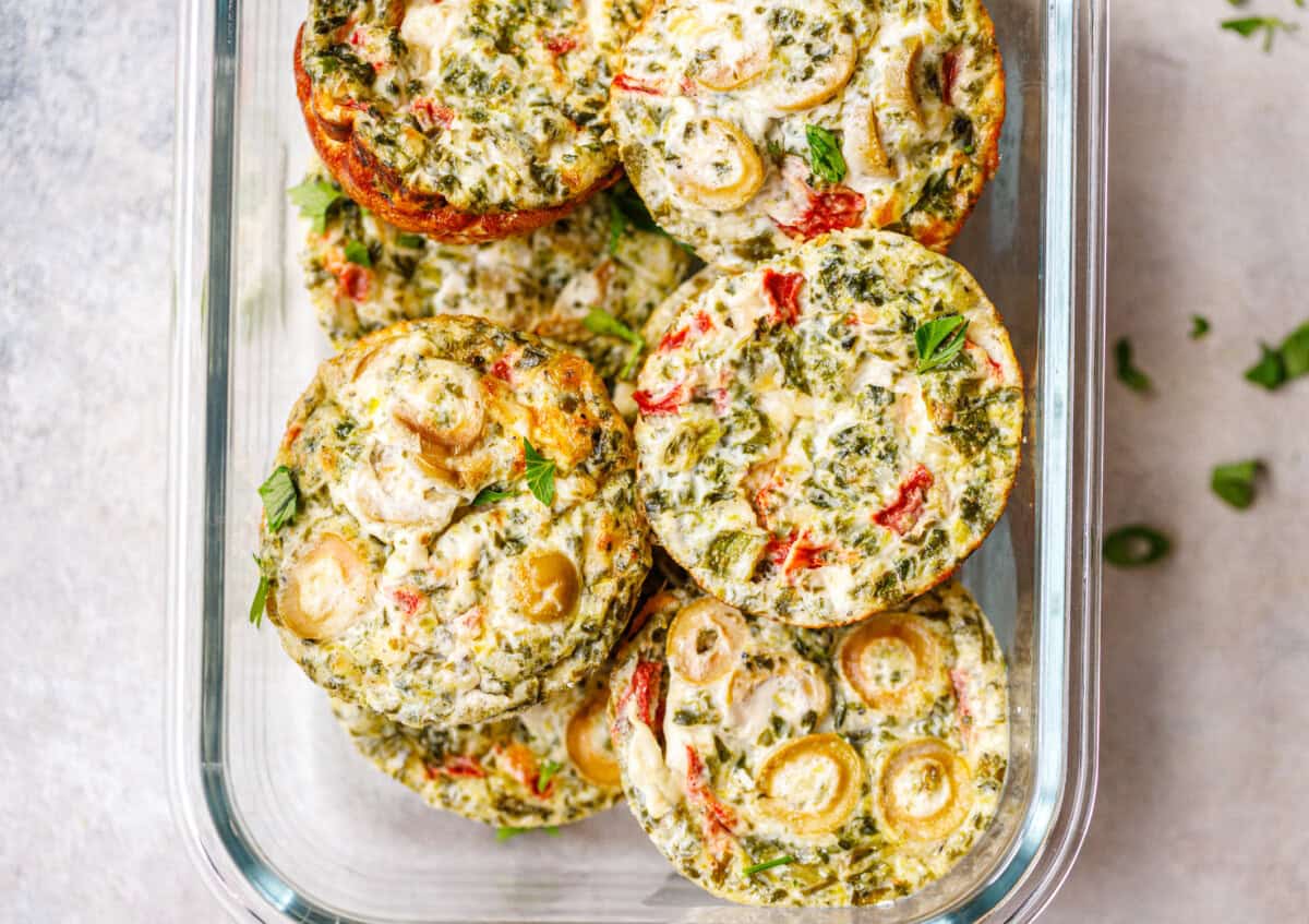 Overhead view of egg white breakfast cups packed in a glass meal prep container, topped with parsley