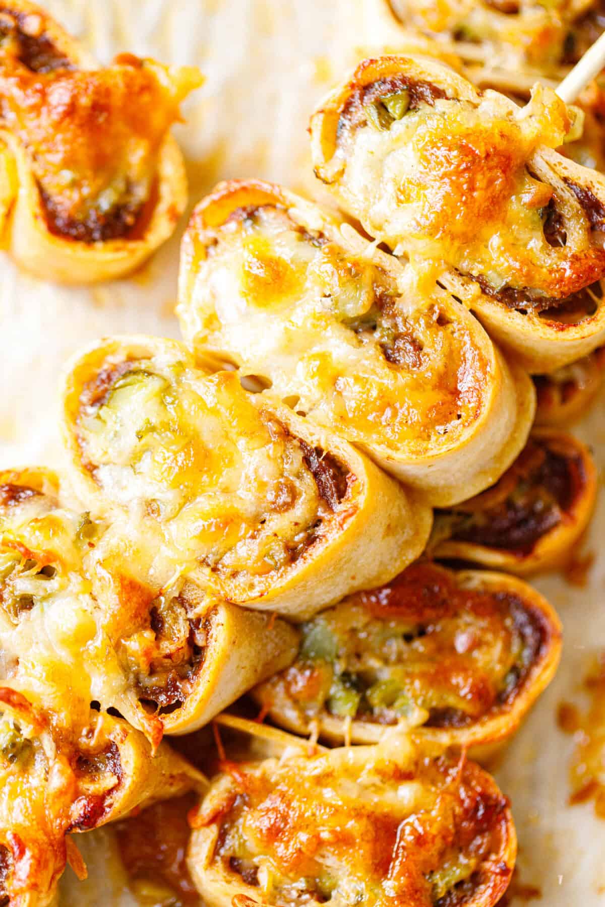 Close-up of baked ground beef tortilla pinwheels with golden melted cheese, showing the spiral of beef and chopped pickles inside.