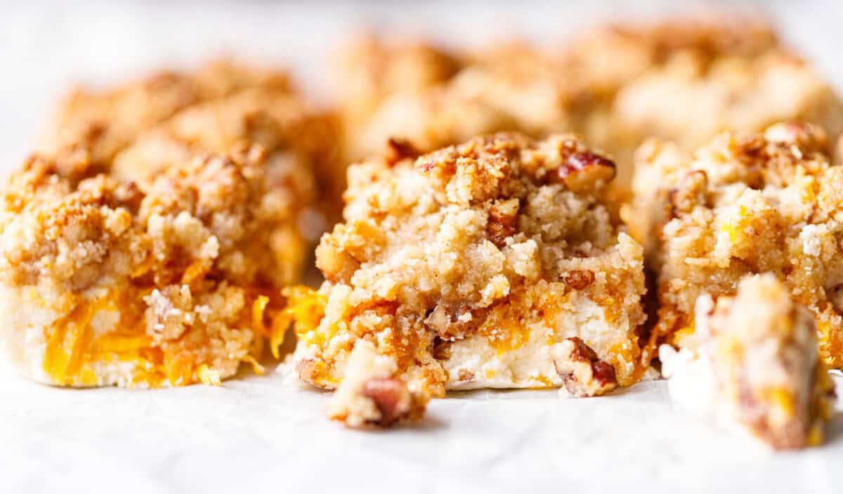 Row of keto pumpkin bars on parchment, the front bar showing its skyr base, orange pumpkin filling and crunchy crumble