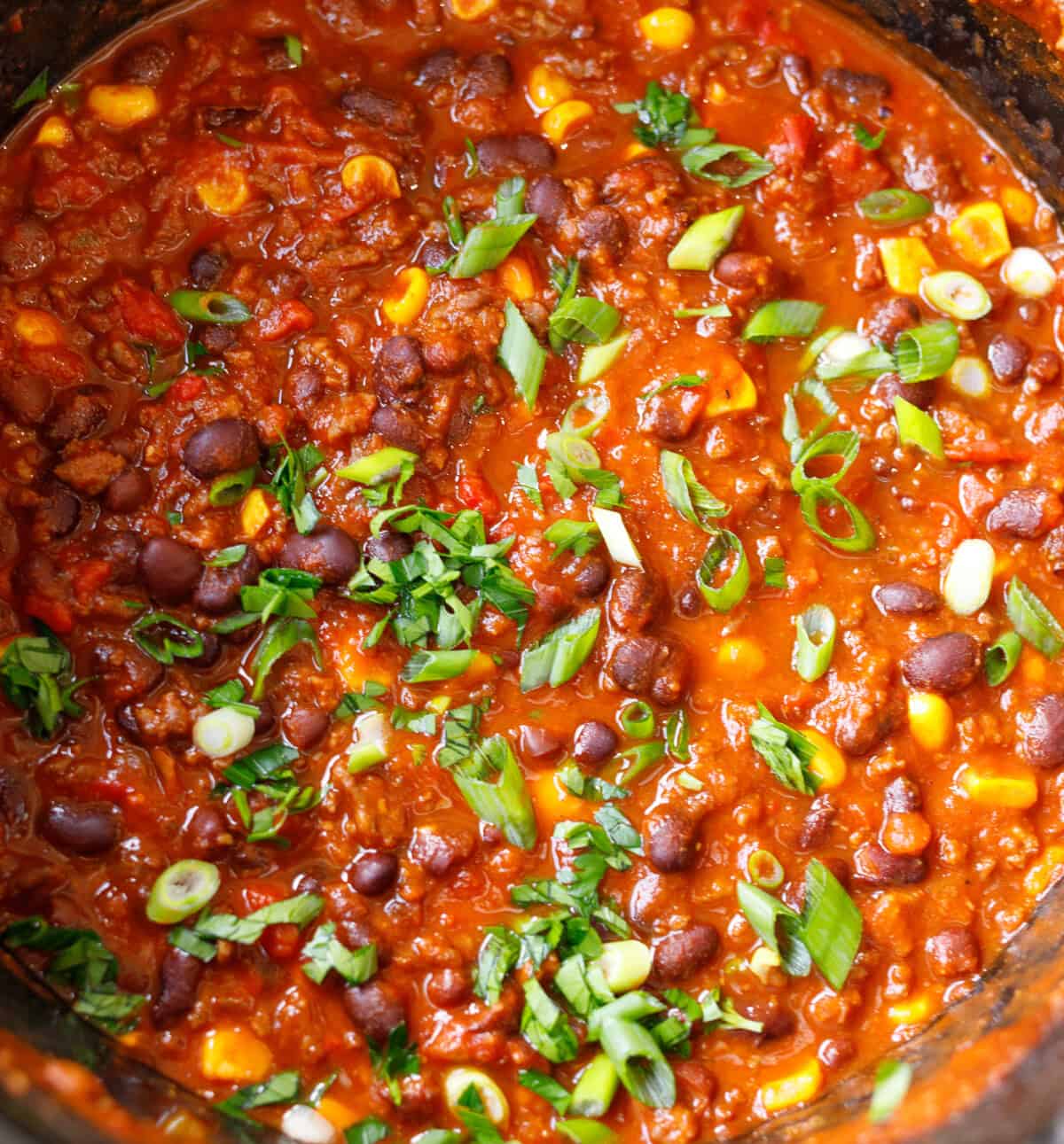 Close-up of finished crockpot chili with ground beef, black and kidney beans, corn, green onion and parsley.