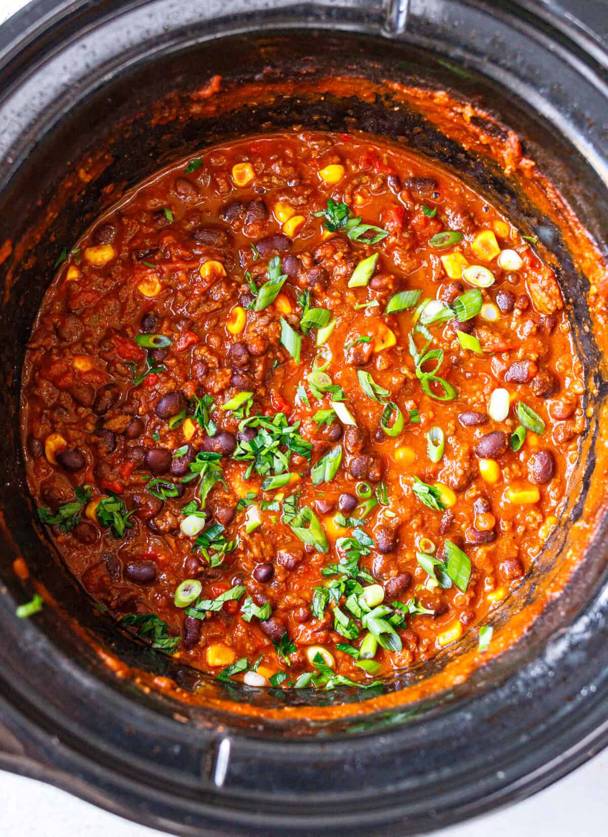 Overhead view of easy crockpot chili in a slow cooker with ground beef, kidney and black beans, corn, green onion and parsley.
