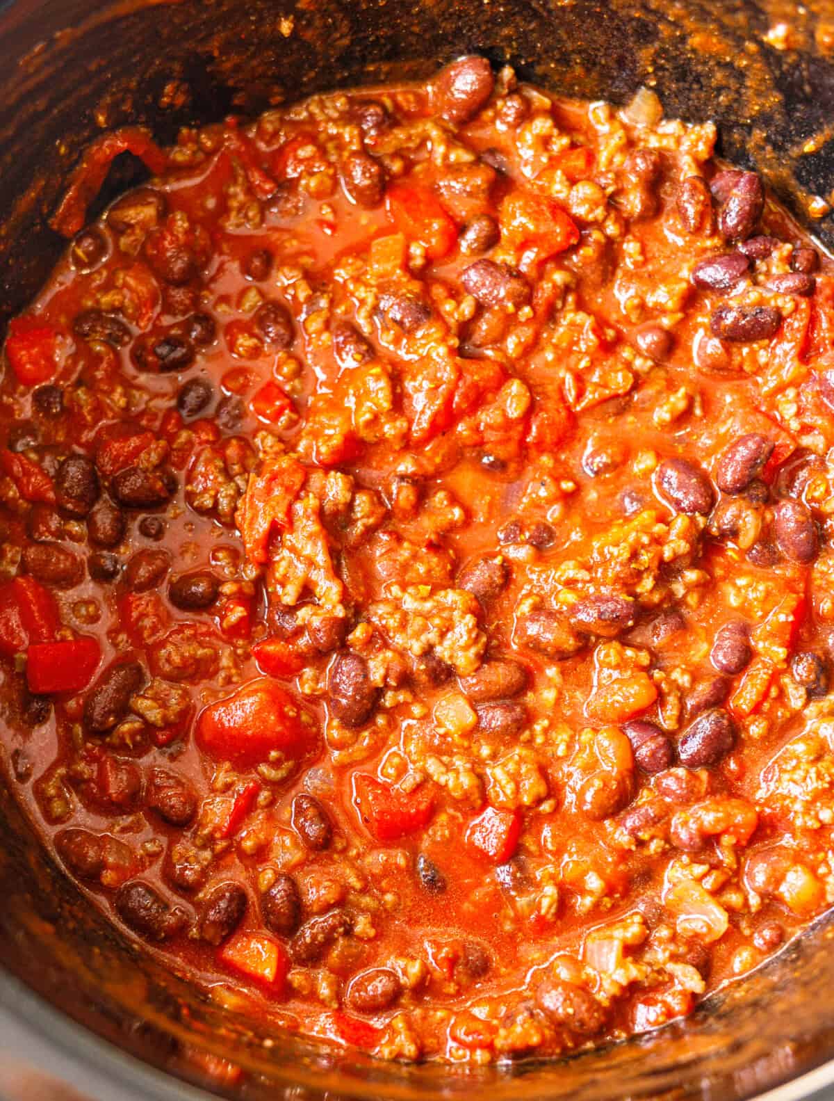 Ground beef, kidney and black beans, red bell pepper and chopped tomatoes in a crockpot before slow cooking.