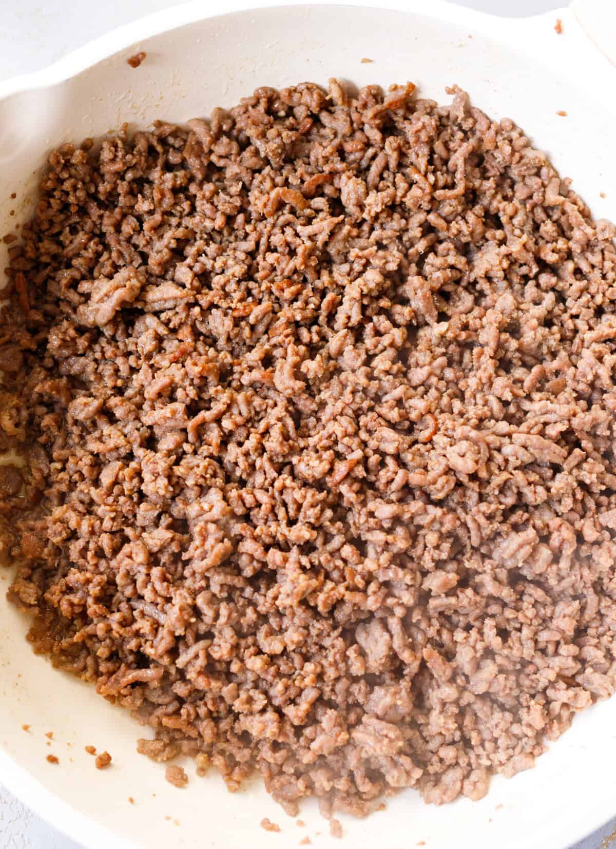 Browned ground beef broken into small crumbles in a white skillet.
