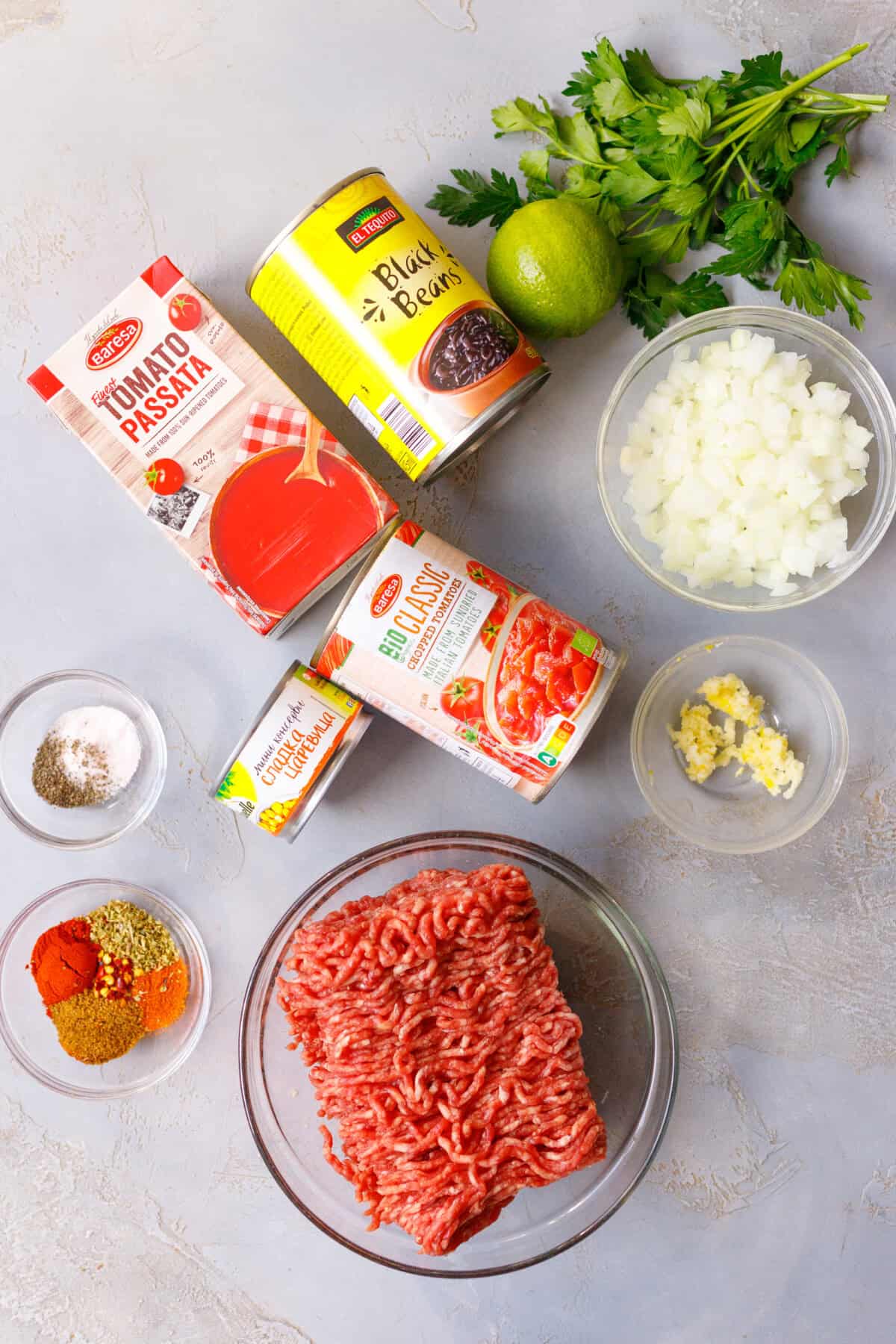 ngredients for easy crockpot chili: ground beef, black beans, chopped tomatoes, tomato passata, corn, diced onion, garlic, spices, lime and parsley.