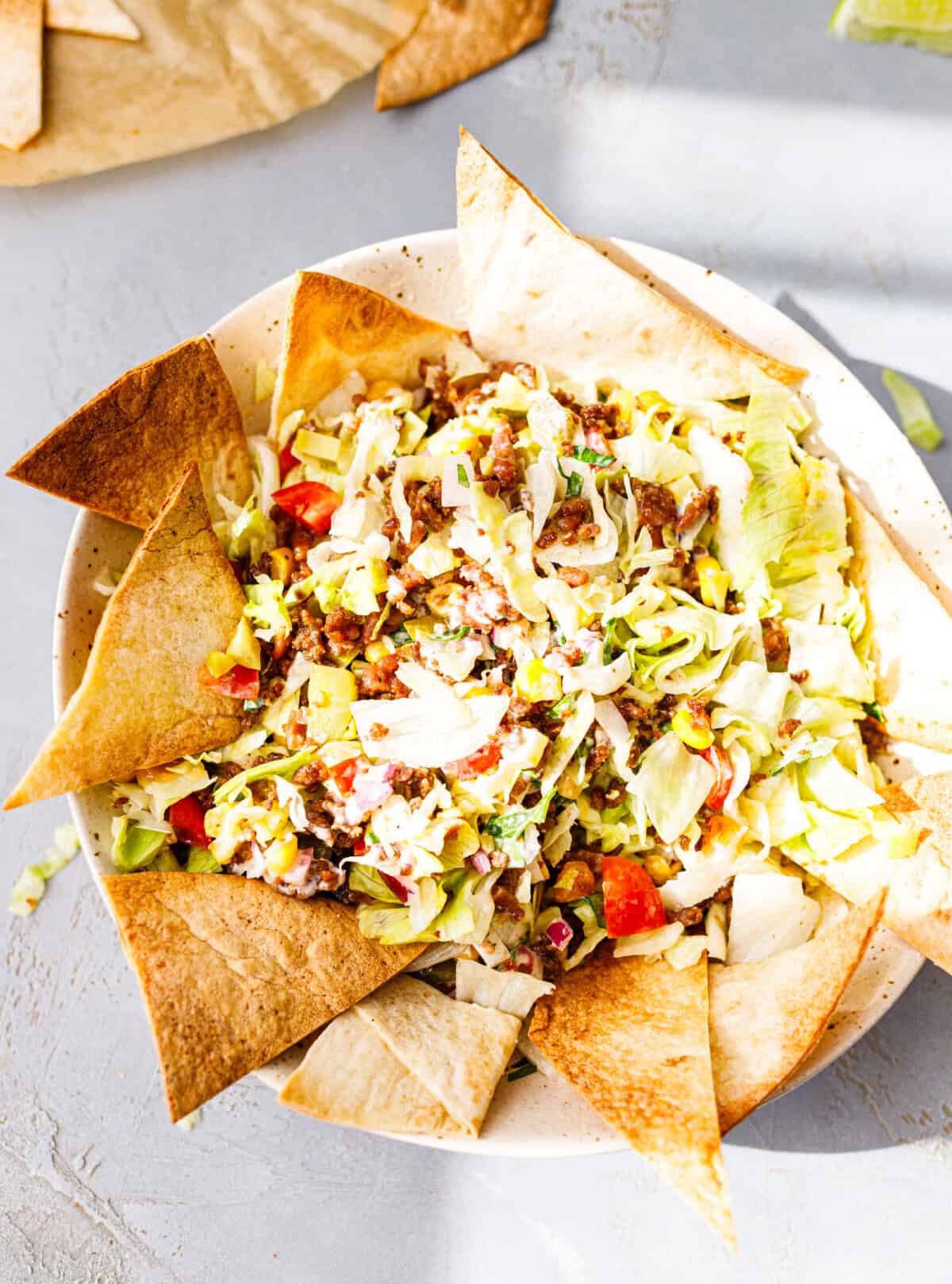 A bowl of easy taco salad with ground beef, iceberg, corn and tomatoes, surrounded by air-fried tortilla chips.