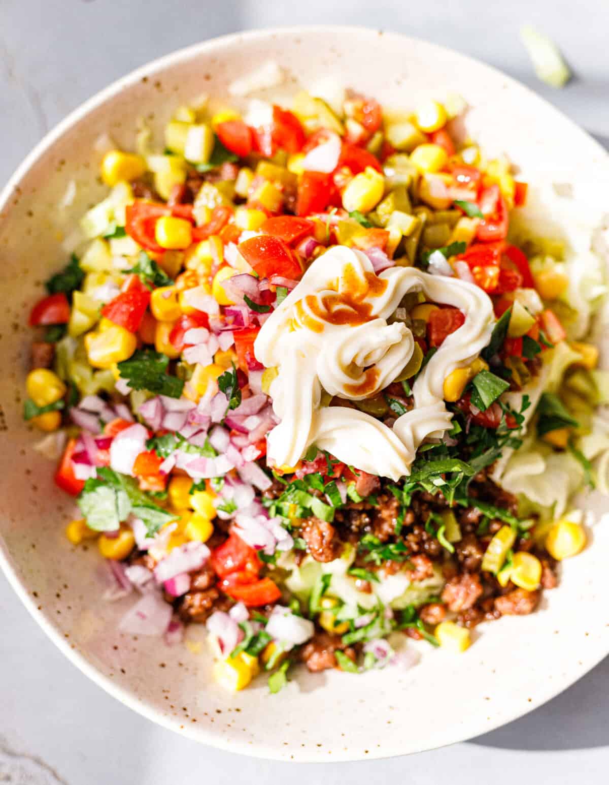 Taco salad with ground beef, corn, tomatoes, red onion, pickles and cilantro, topped with a creamy dressing and Cholula hot sauce before tossing.