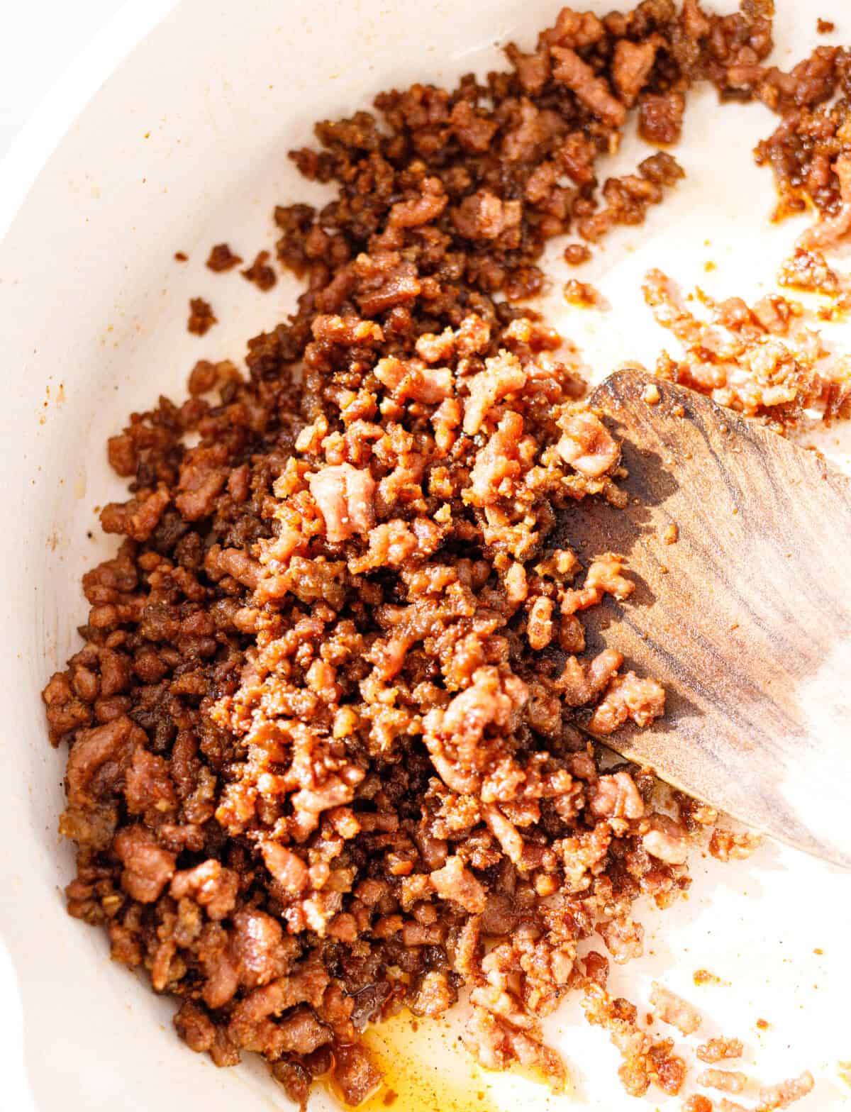Crispy seasoned ground beef with paprika, cumin and garlic powder in a skillet with a wooden spatula.