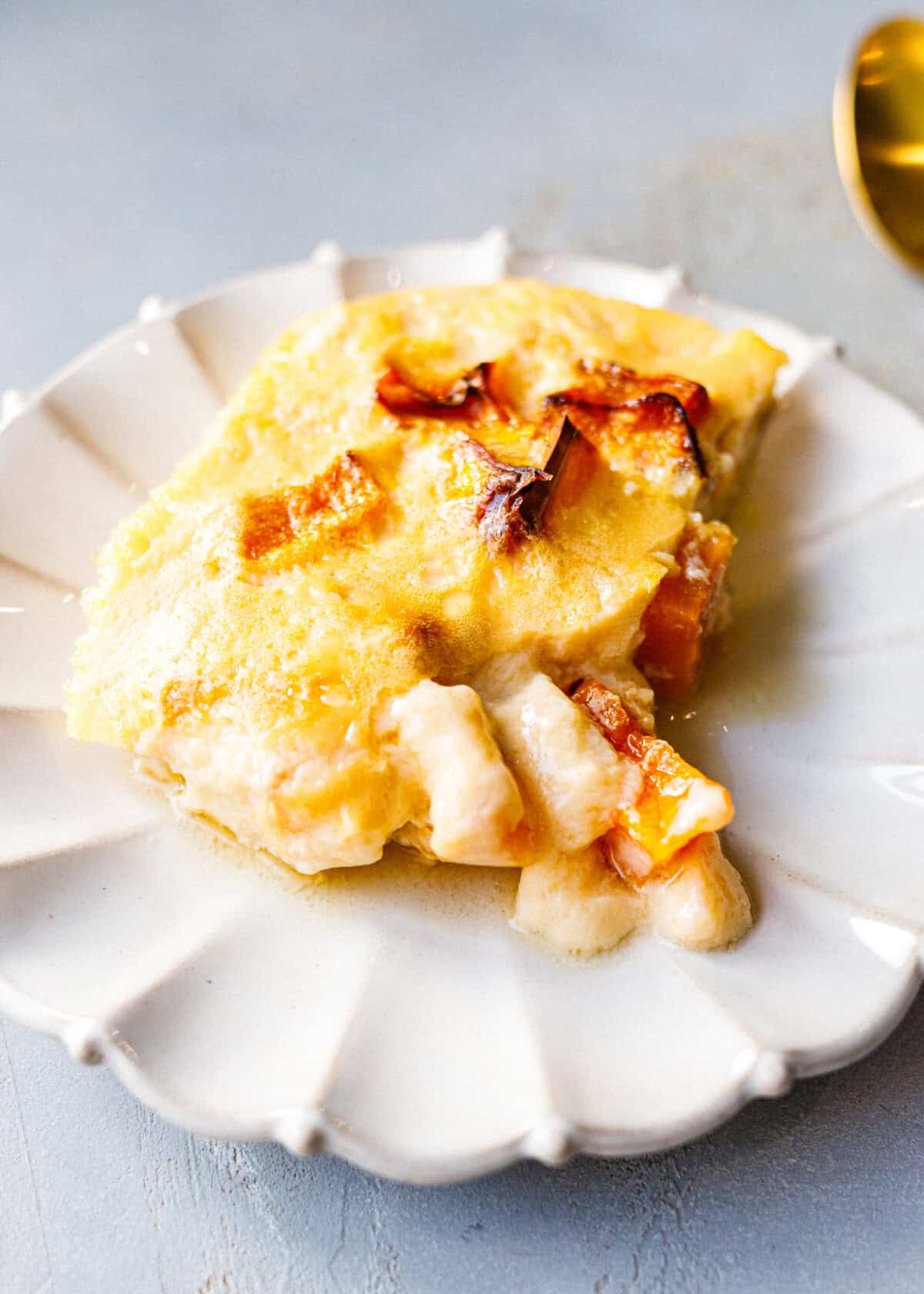 A square of low-carb baked pumpkin custard on a scalloped white plate, with caramelized pumpkin pieces on top.
