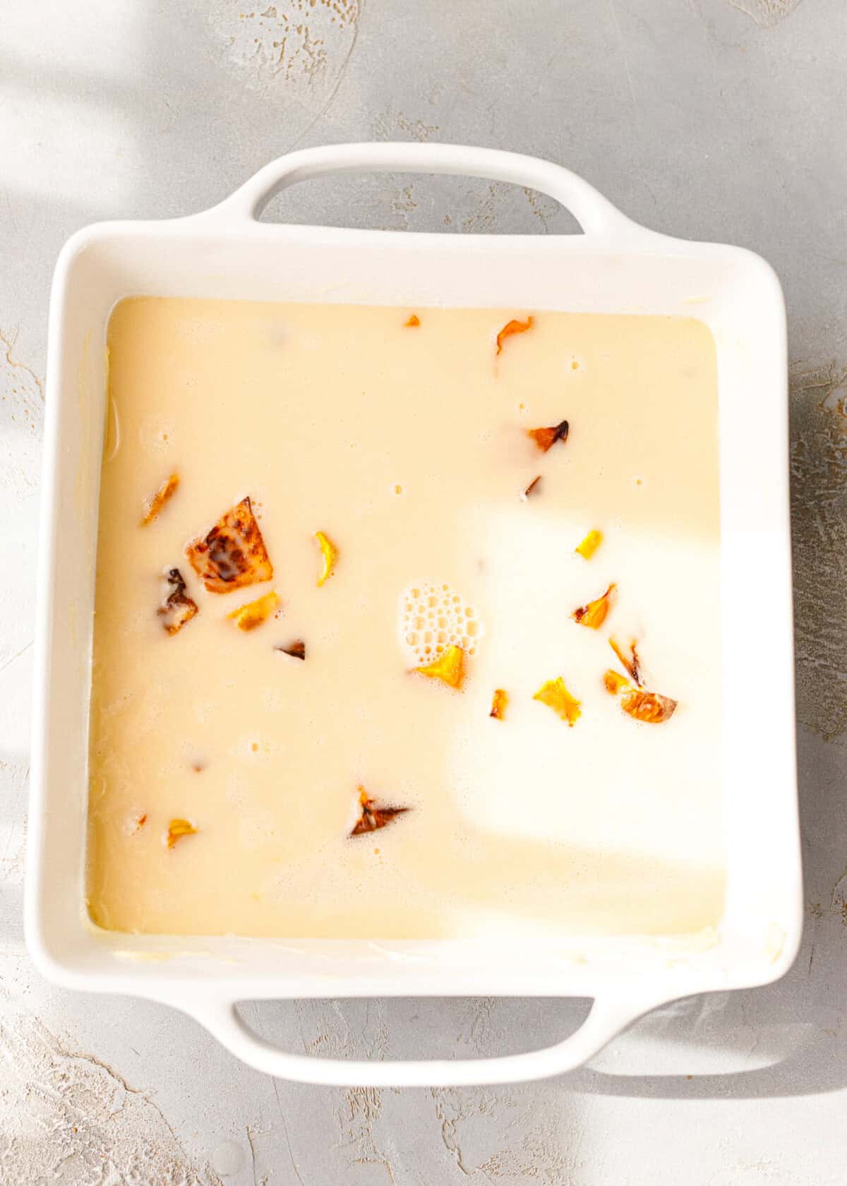 Custard mixture poured over roasted pumpkin pieces in a square white baking dish before baking.