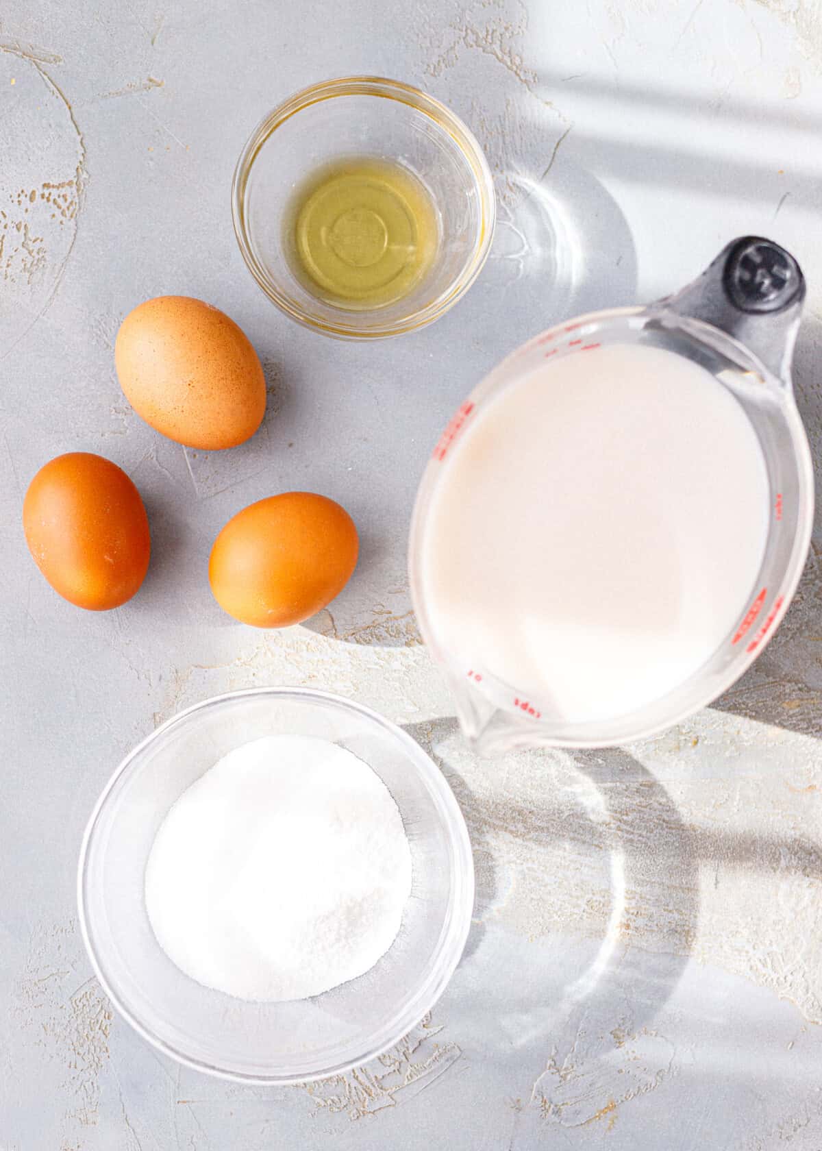 Ingredients for baked pumpkin custard: three eggs, almond milk in a measuring cup, monk fruit sweetener and vanilla.