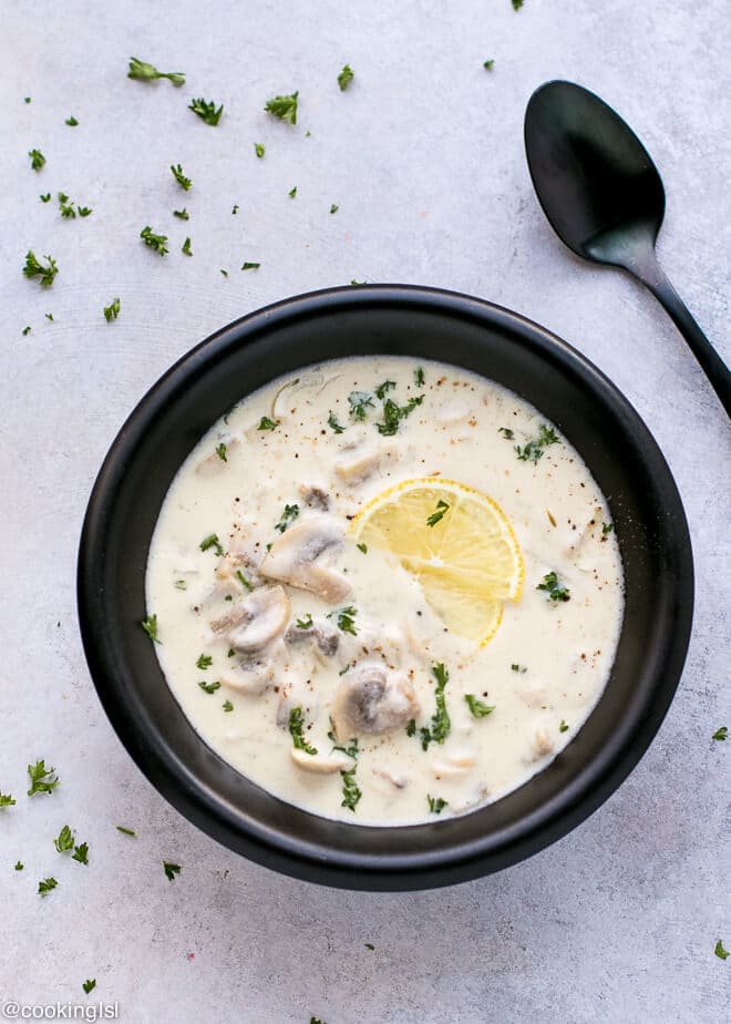 A black ceramic bowl, with Creamy Mushroom Soup Recipe (Wolfgang Puck Copycat) and a spoon on the side. Zesty and delicious!
