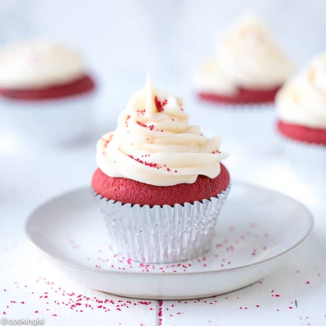 Easy Red Velvet Cupcakes Recipe on a white plate topped with red sprinkles.