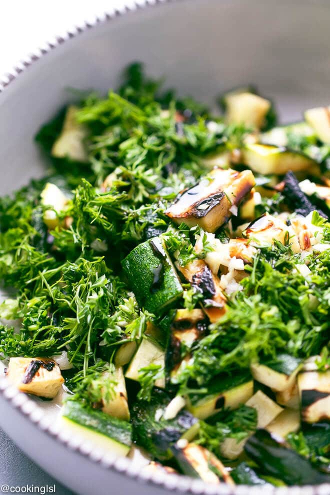 A bowl with grilled zucchini salad, cut lengthwise, topped with fresh chopped dill, parsley, garlic, olive oil, balsamic and apple cider vinegar. Bulgarian zucchini salad.
