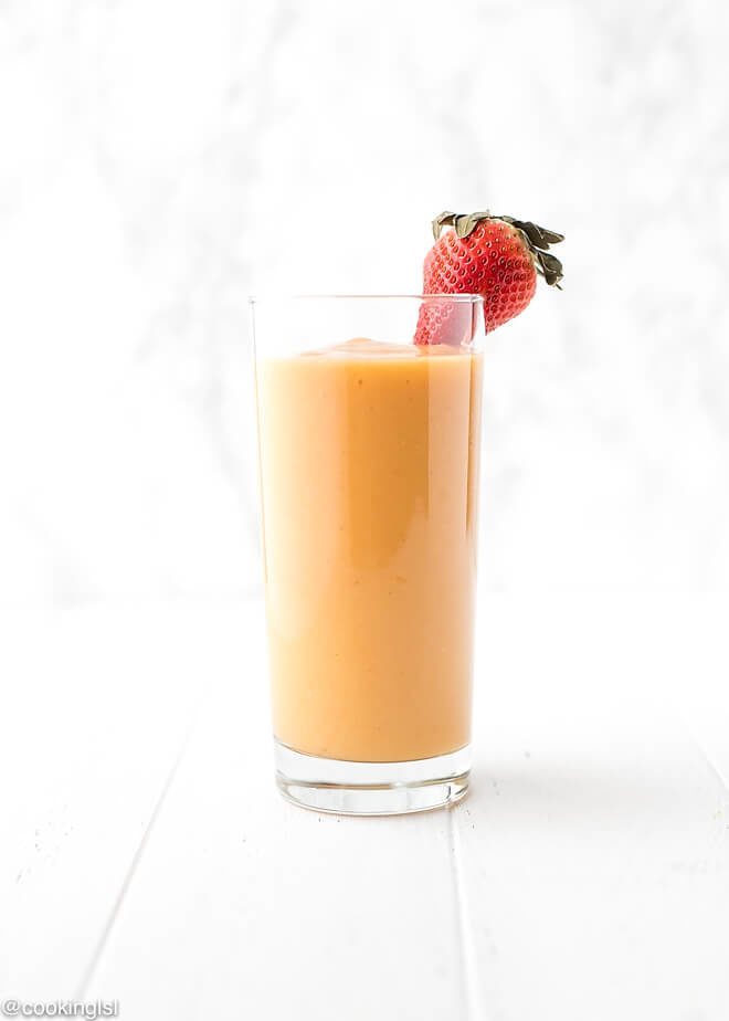 This strawberry mango smoothie i in a tall clear glass with a straw, tropical flavor and color