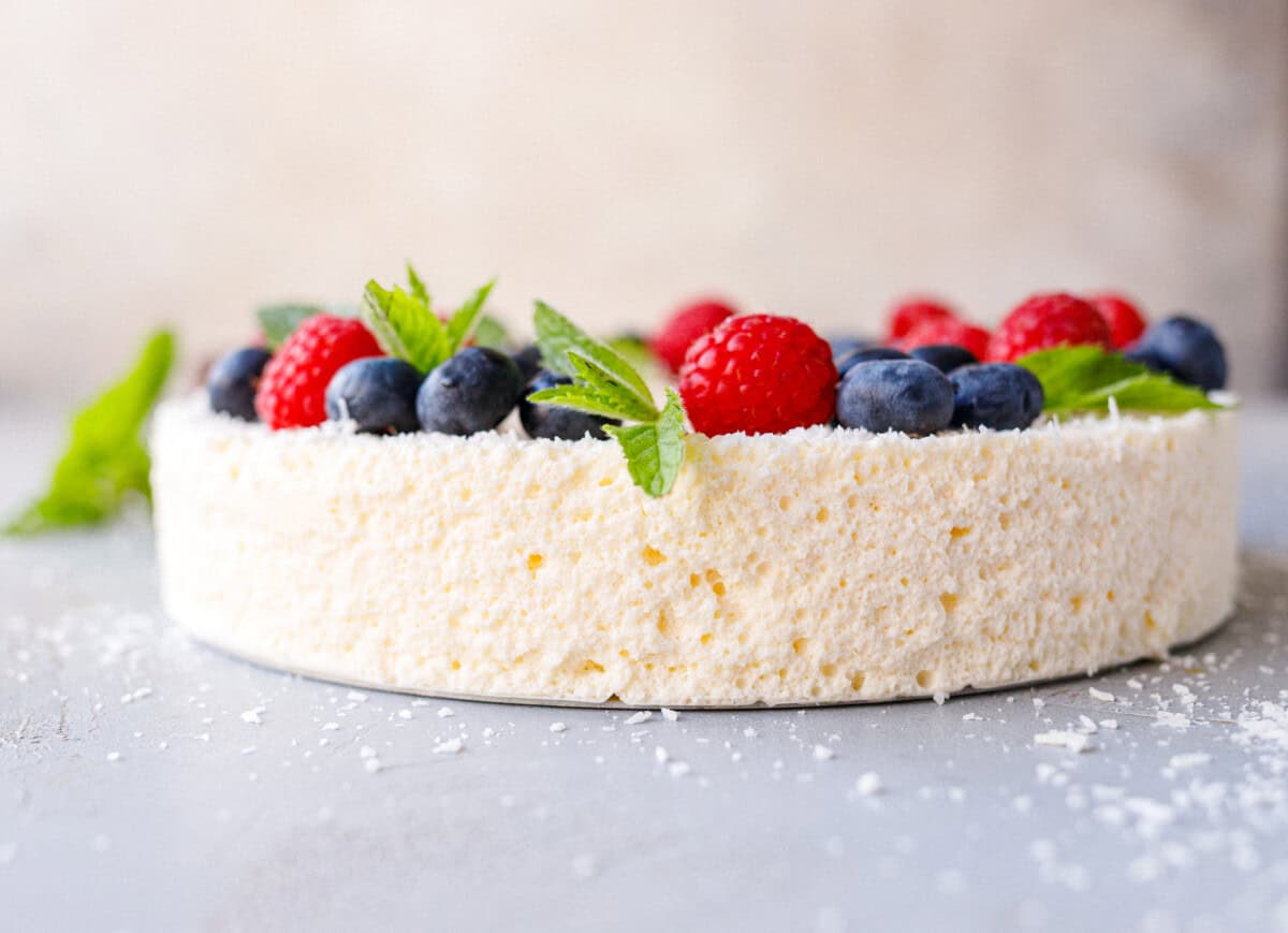 Side view of a no bake yogurt cake showing the airy gelatin-set texture, topped with berries and mint