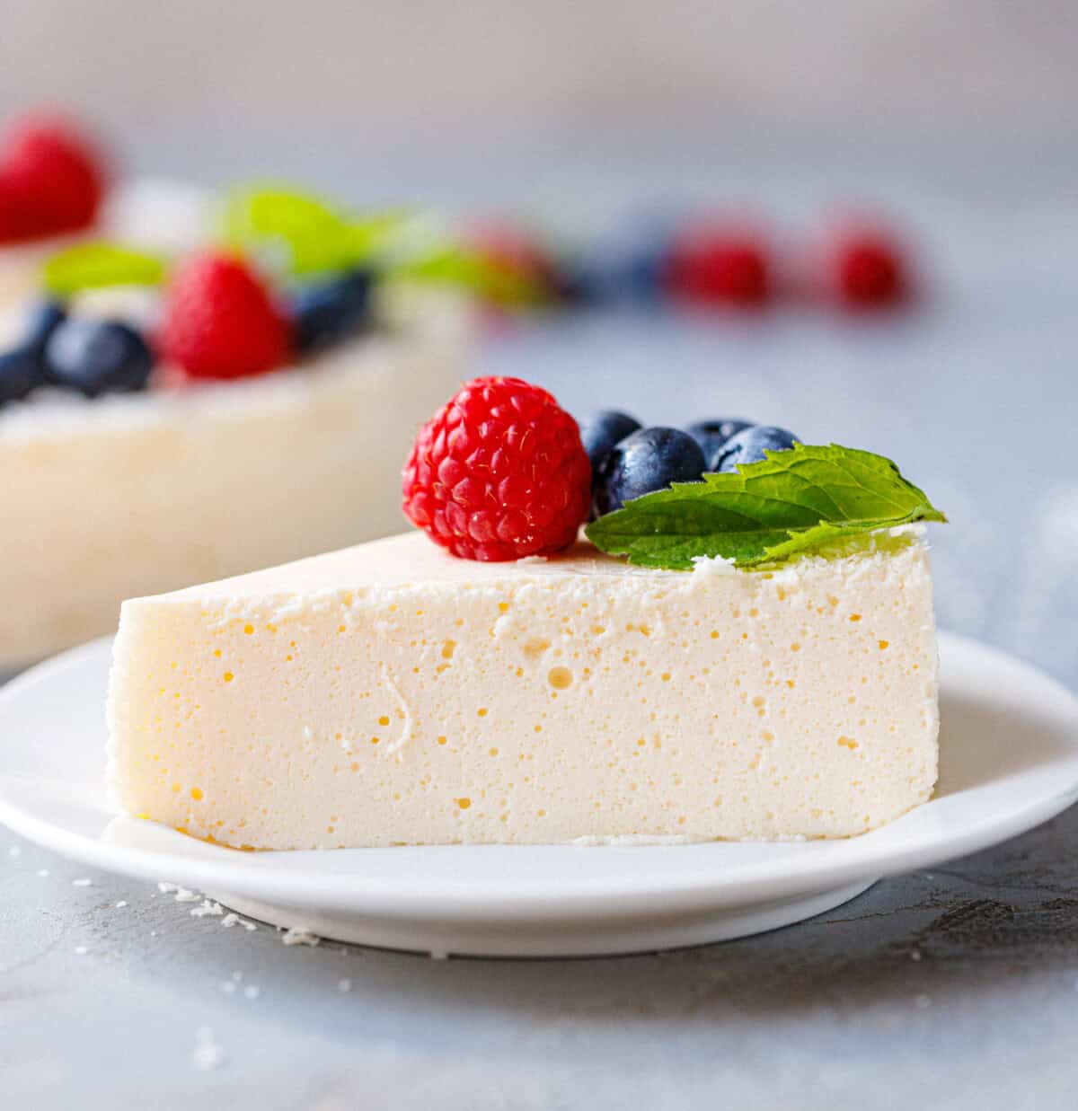 Slice of no bake yogurt cake topped with fresh raspberries, blueberries and mint on a white plate