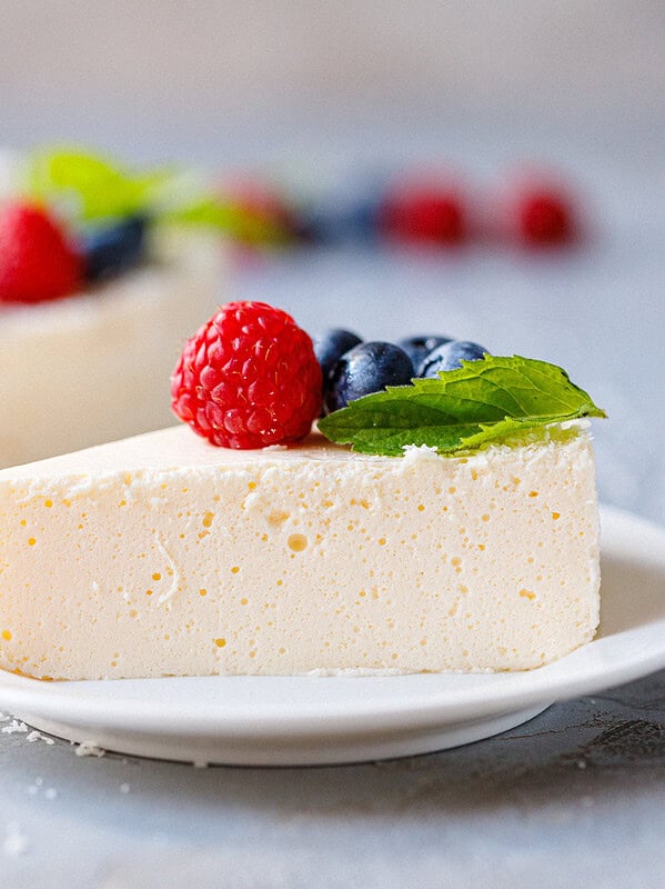 Slice of no bake yogurt cake topped with fresh raspberries, blueberries and mint on a white plate