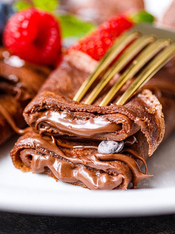 2 chocolate crepes with chocolate filling on a plate on top of each other