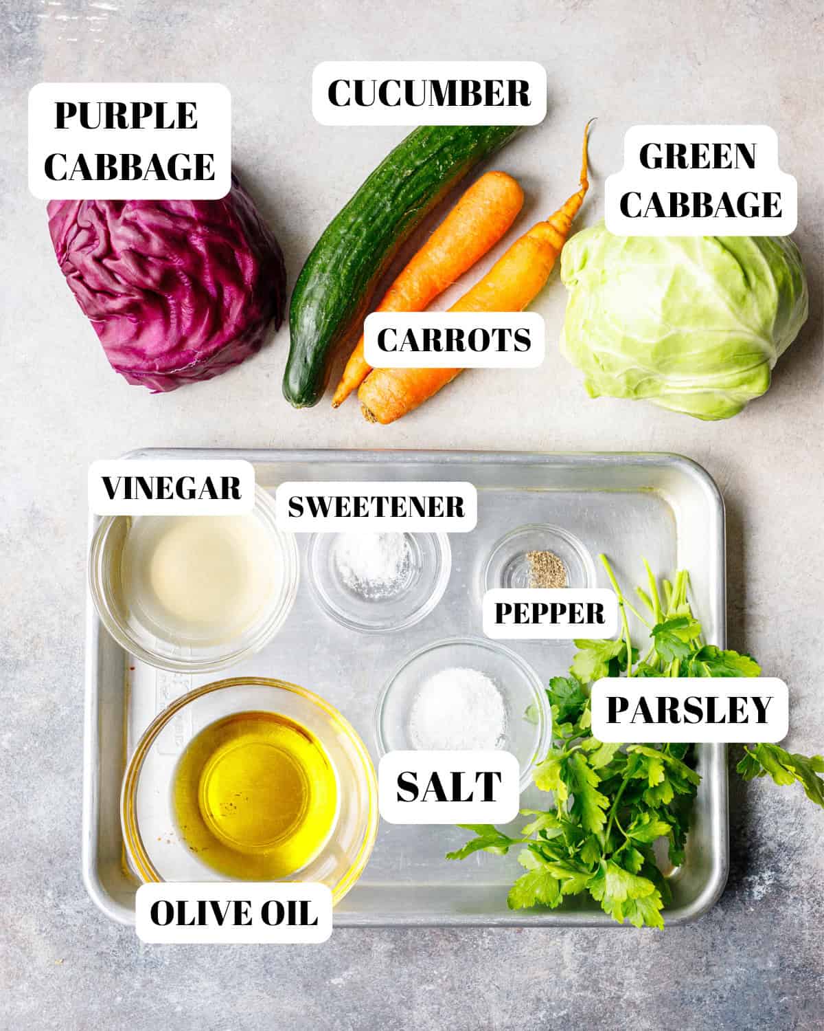 Ingredients for cabbage salad including green cabbage, purple cabbage, cucumber, carrots, olive oil, vinegar, parsley, salt, pepper, and sweetener