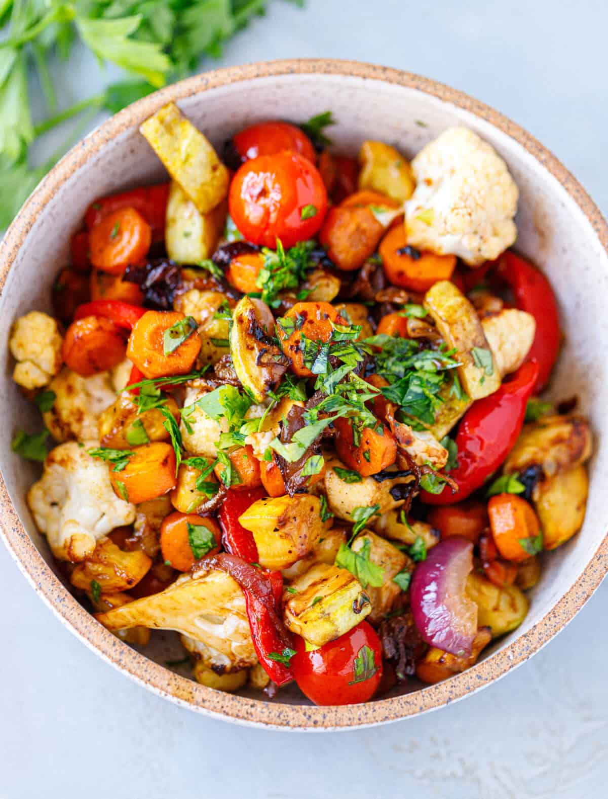 Overhead bowl of grilled vegetables with balsamic, topped with chopped fresh parsley and basil