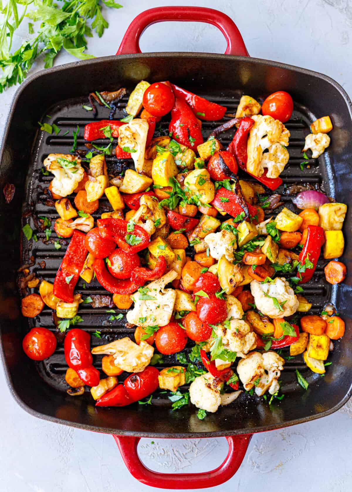 Balsamic grilled vegetables in a red cast iron grill pan topped with chopped fresh parsley