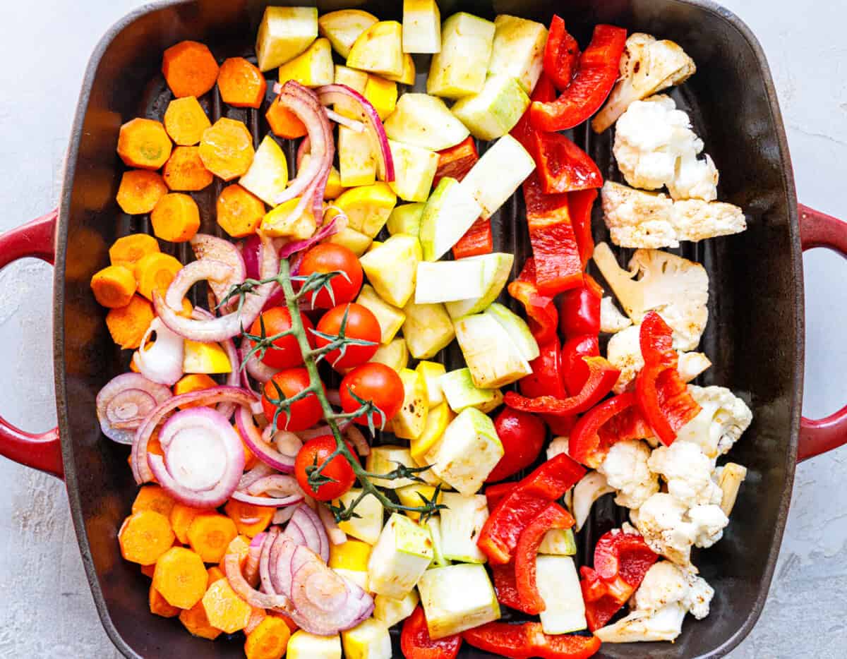 Raw carrots, zucchini, red onion, cherry tomatoes, red pepper and cauliflower arranged in a grill pan