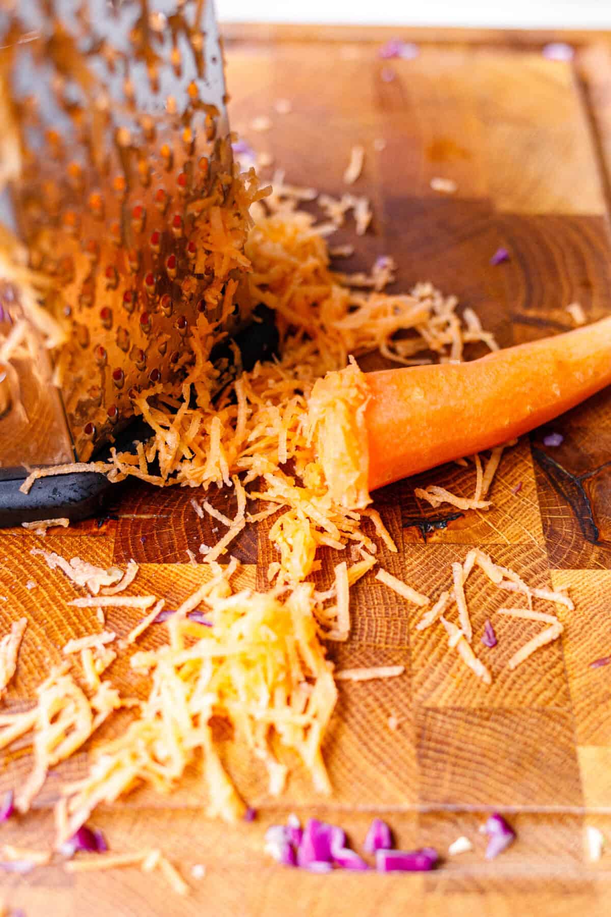 Grating fresh carrot on a box grater over a wooden cutting board for cabbage salad