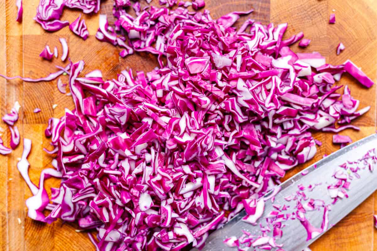 Finely chopped purple cabbage on a wooden cutting board with a knife