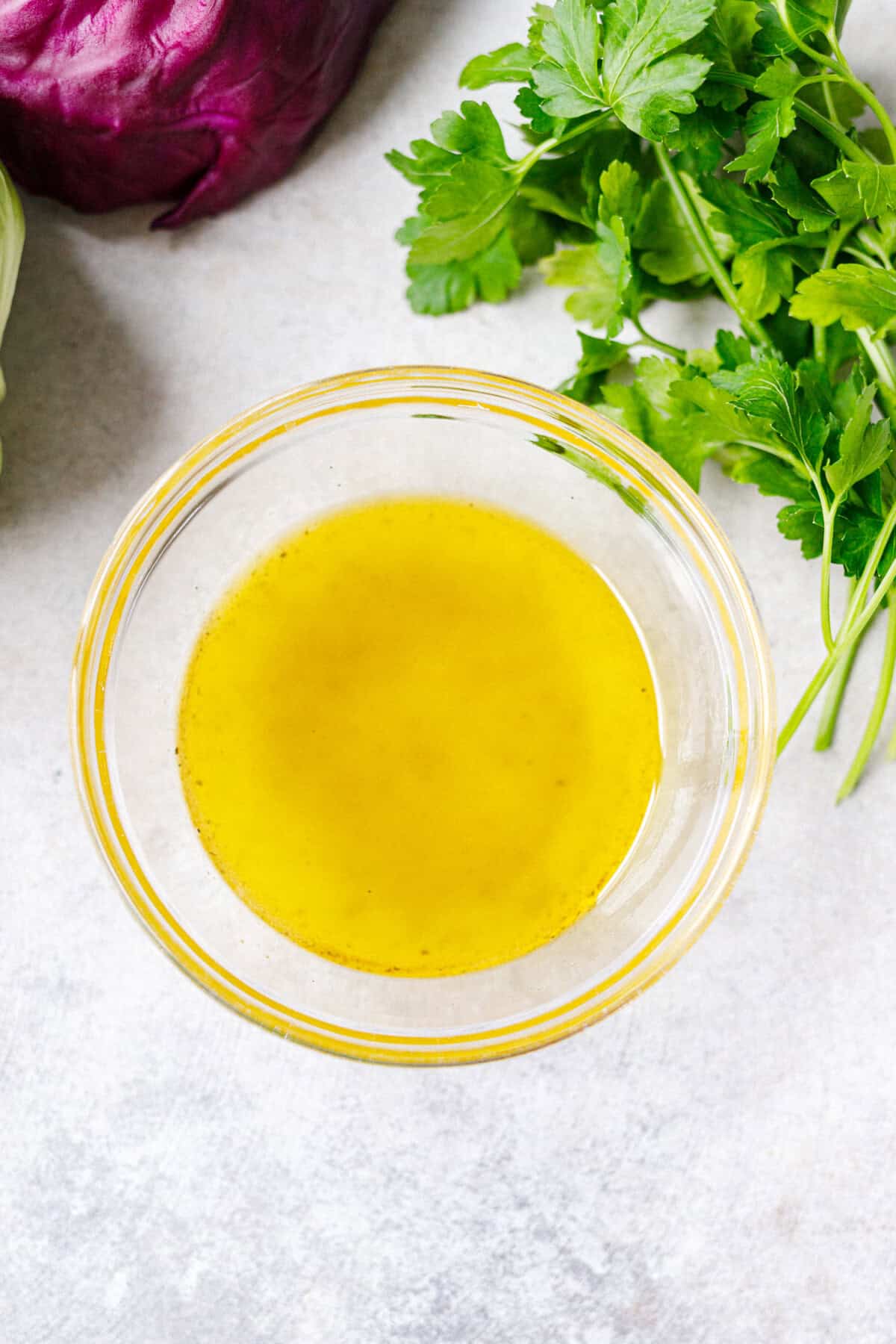 Simple homemade salad dressing with olive oil and vinegar in a glass bowl with fresh parsley