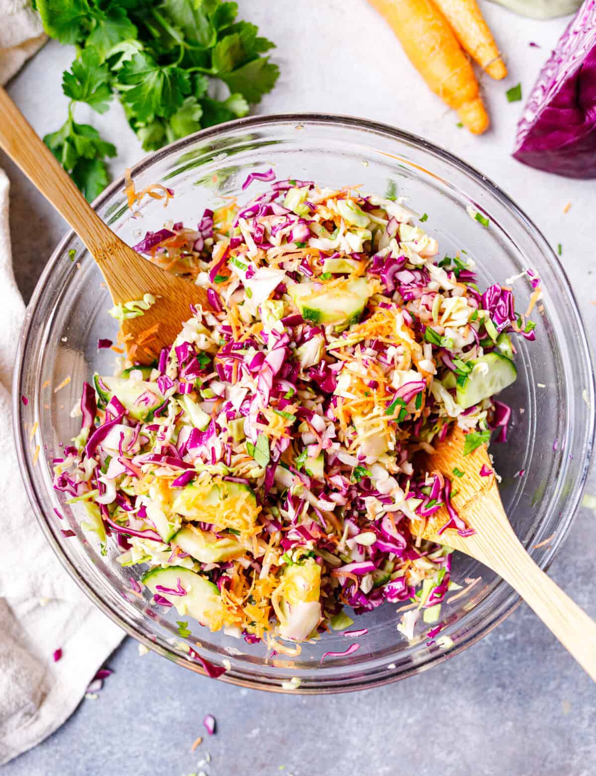 Mixing cabbage salad in a glass bowl with wooden spoon, combining cabbage, cucumber, and carrots
