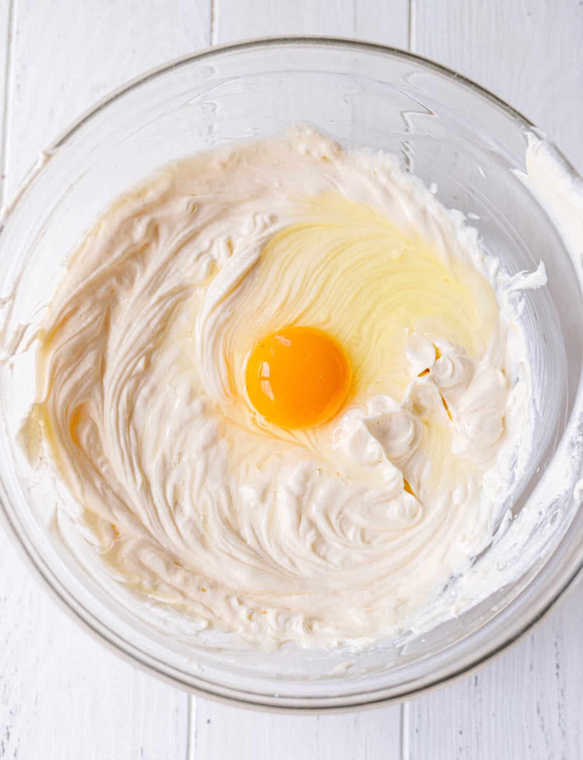 A whole egg being added to cream cheese filling in a glass bowl