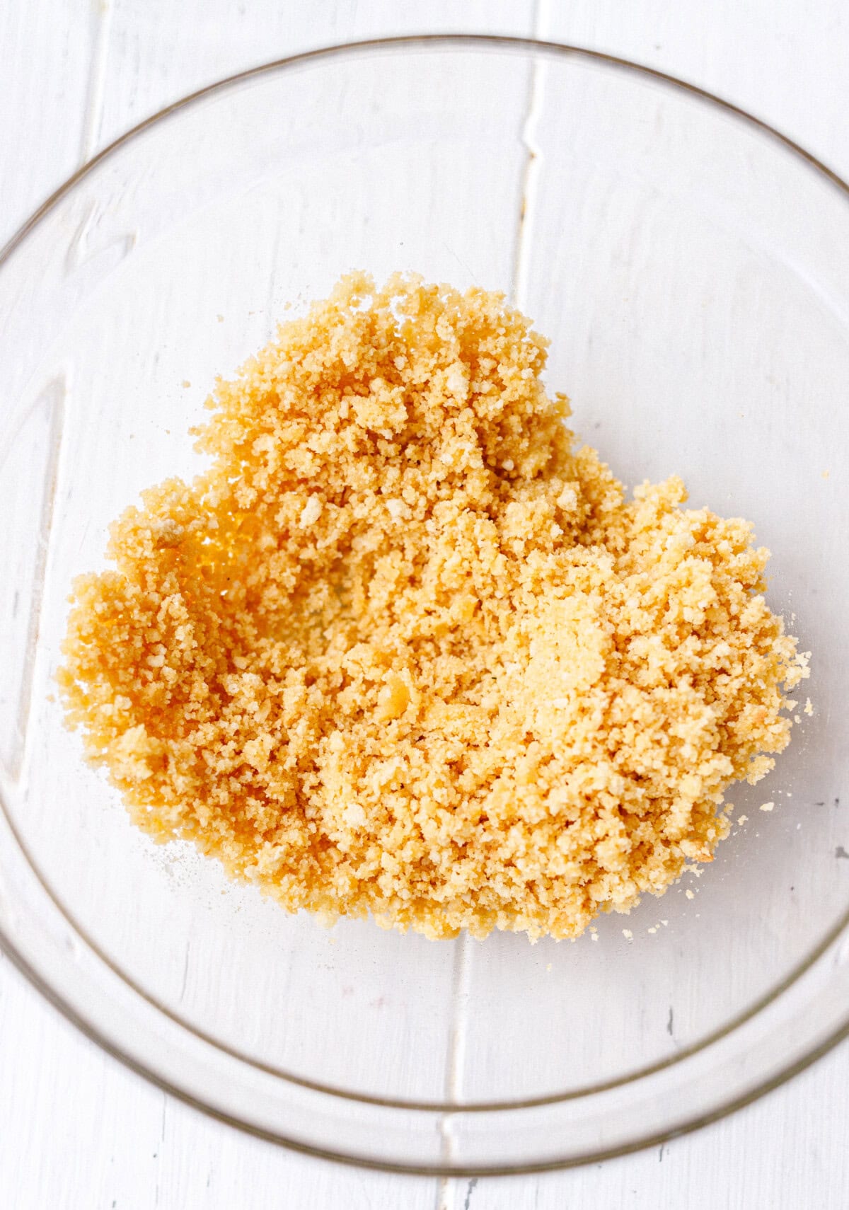 Graham cracker crumbs mixed with melted butter in a glass bowl on a white surface
