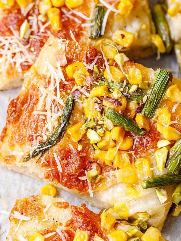 Close-up of asparagus corn pizza slices topped with corn kernels, chopped pistachios, and shredded parmesan on golden crispy crust