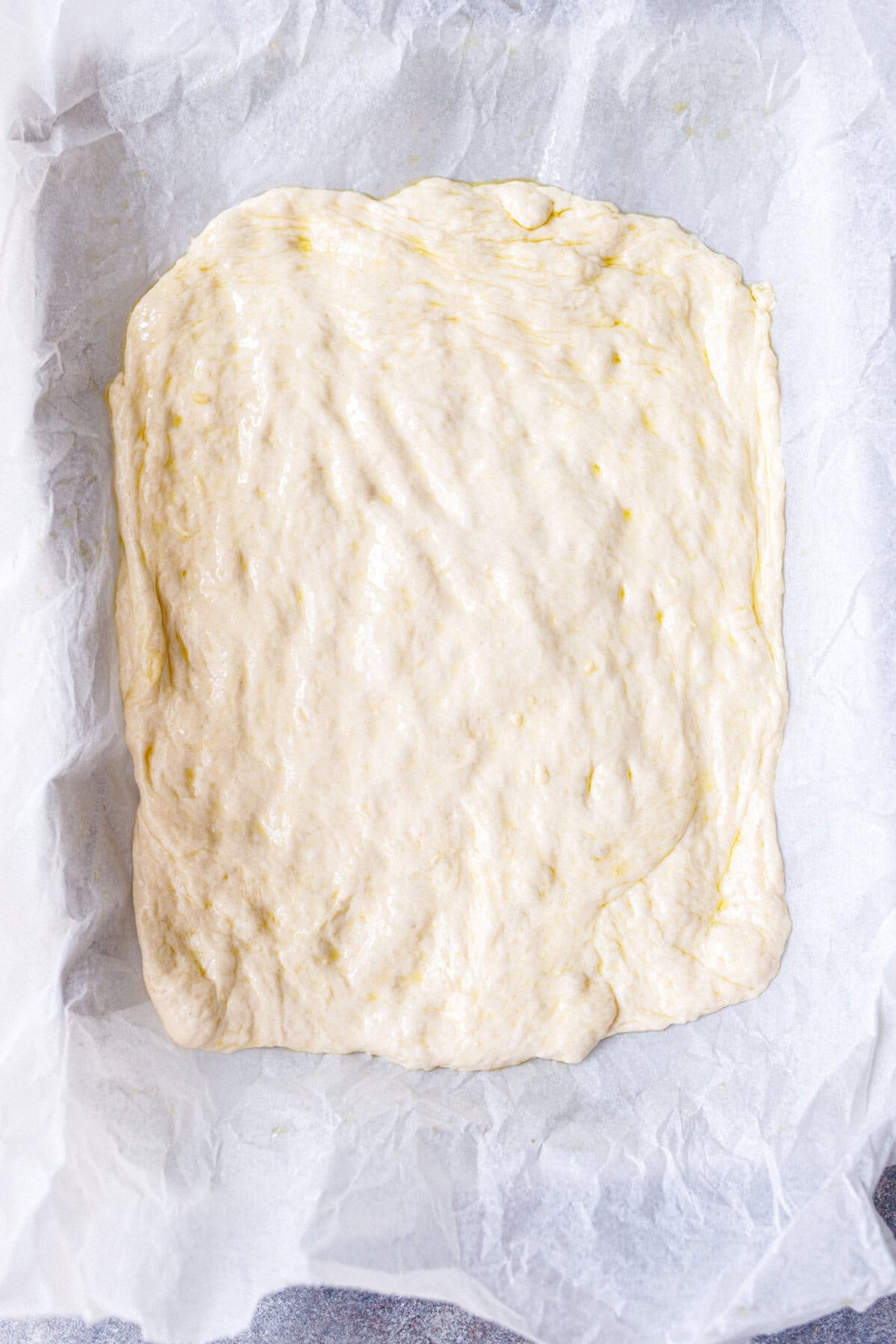 Homemade pizza dough stretched thin in a parchment-lined 9x13 inch pan before toppings