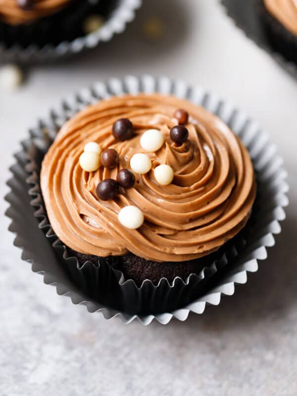 eggless chocolate cupcake with Prague frosting piped on top and chocolate sprinkles in a black liner