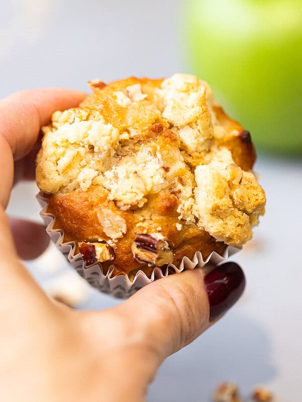 Hand holding an apple oat muffin with a buttery crumb topping and chopped pecans Title: Apple Oat Muffin in Hand