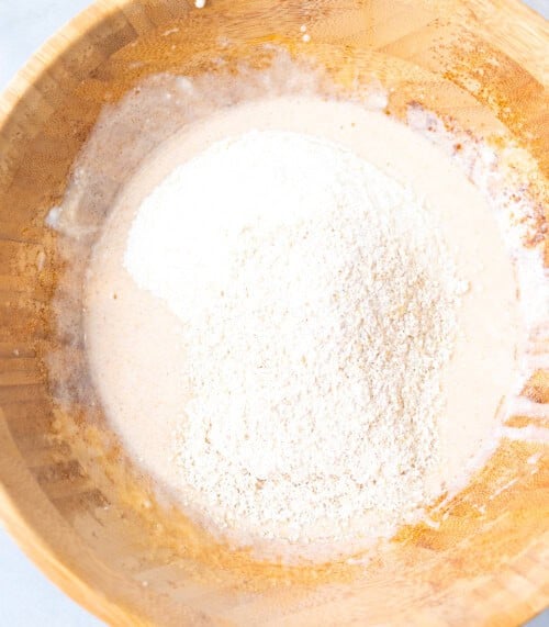 Oat flour and all-purpose flour added to the wet ingredients in a wooden bowl