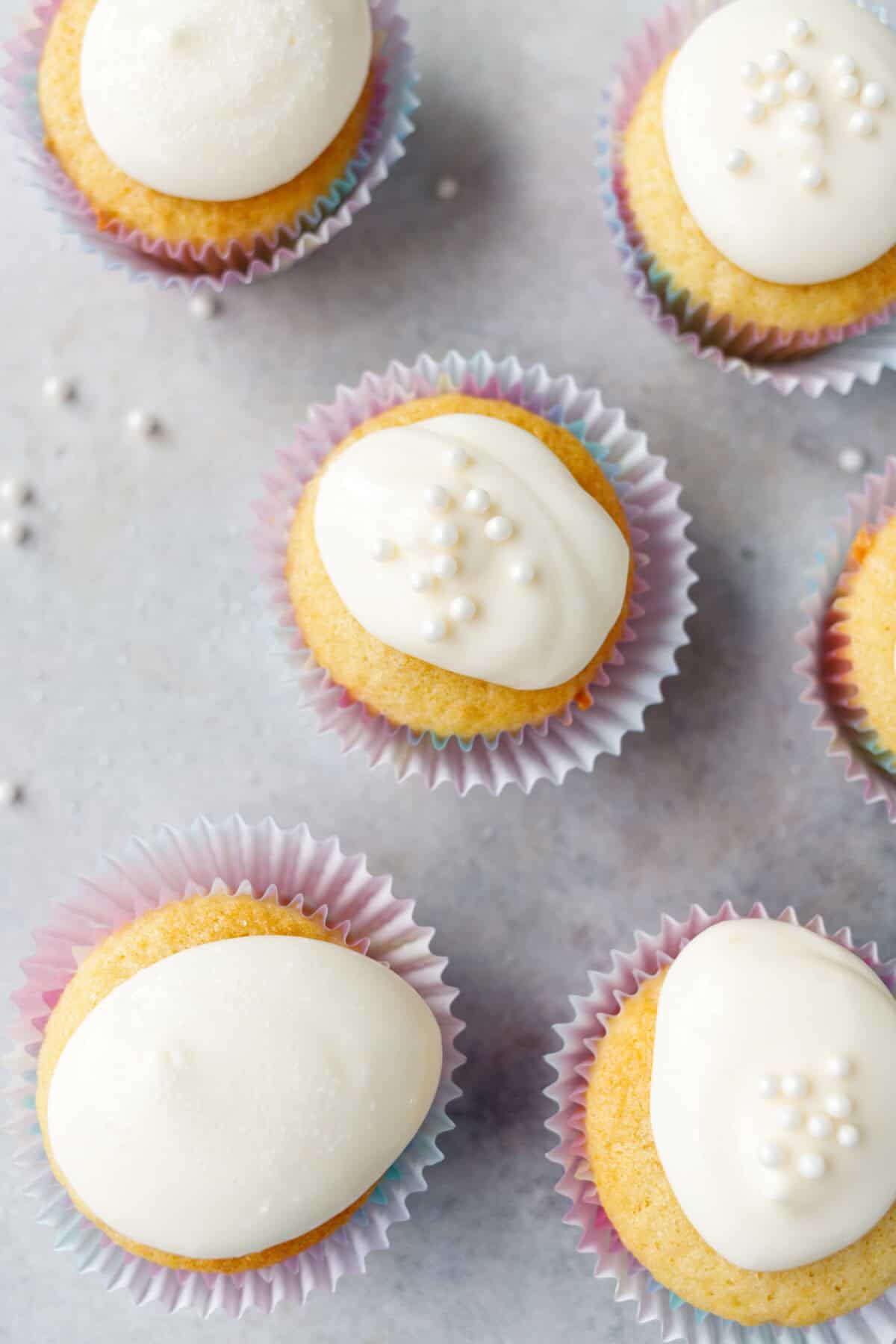 Vanilla cupcakes with white frosting arranged on a light surface with sprinkles