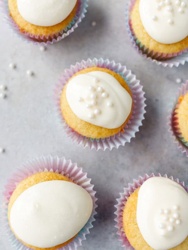 Vanilla cupcakes with white frosting arranged on a light surface with sprinkles