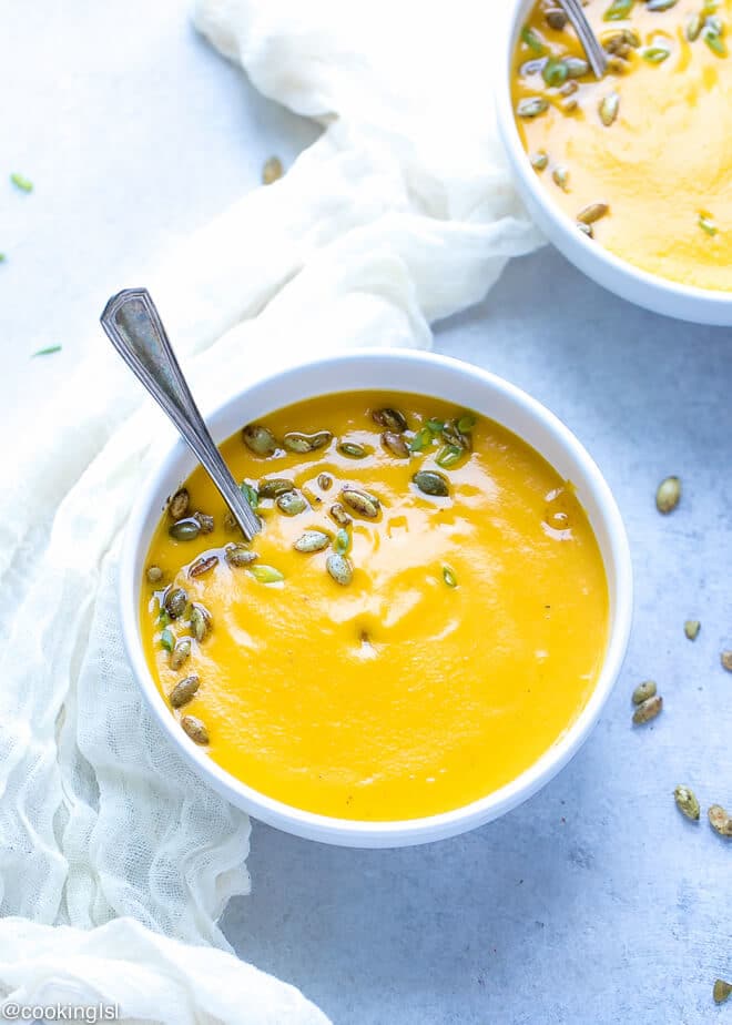 A white bowl with roasted butternut squash soup, with a spoon and topped with pumpkin seeds.