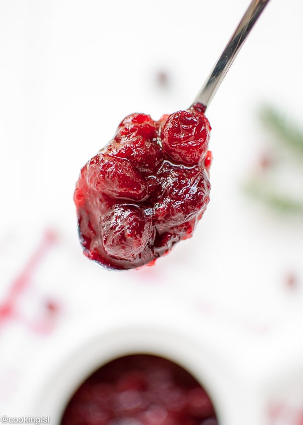 A ceramic dish filled with Easy Homemade Cranberry Sauce. A spoon full of cranberry sauce.