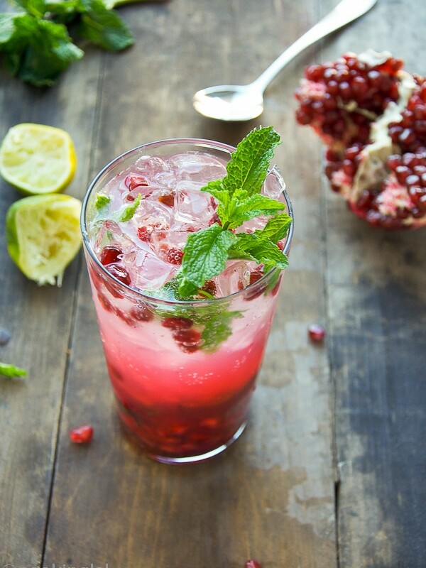 Winter NYE Pomegranate Mojito Cocktail, in a tall clear glass, with pomegranate seeds, lime juice, simple syrup and fresh mint.
