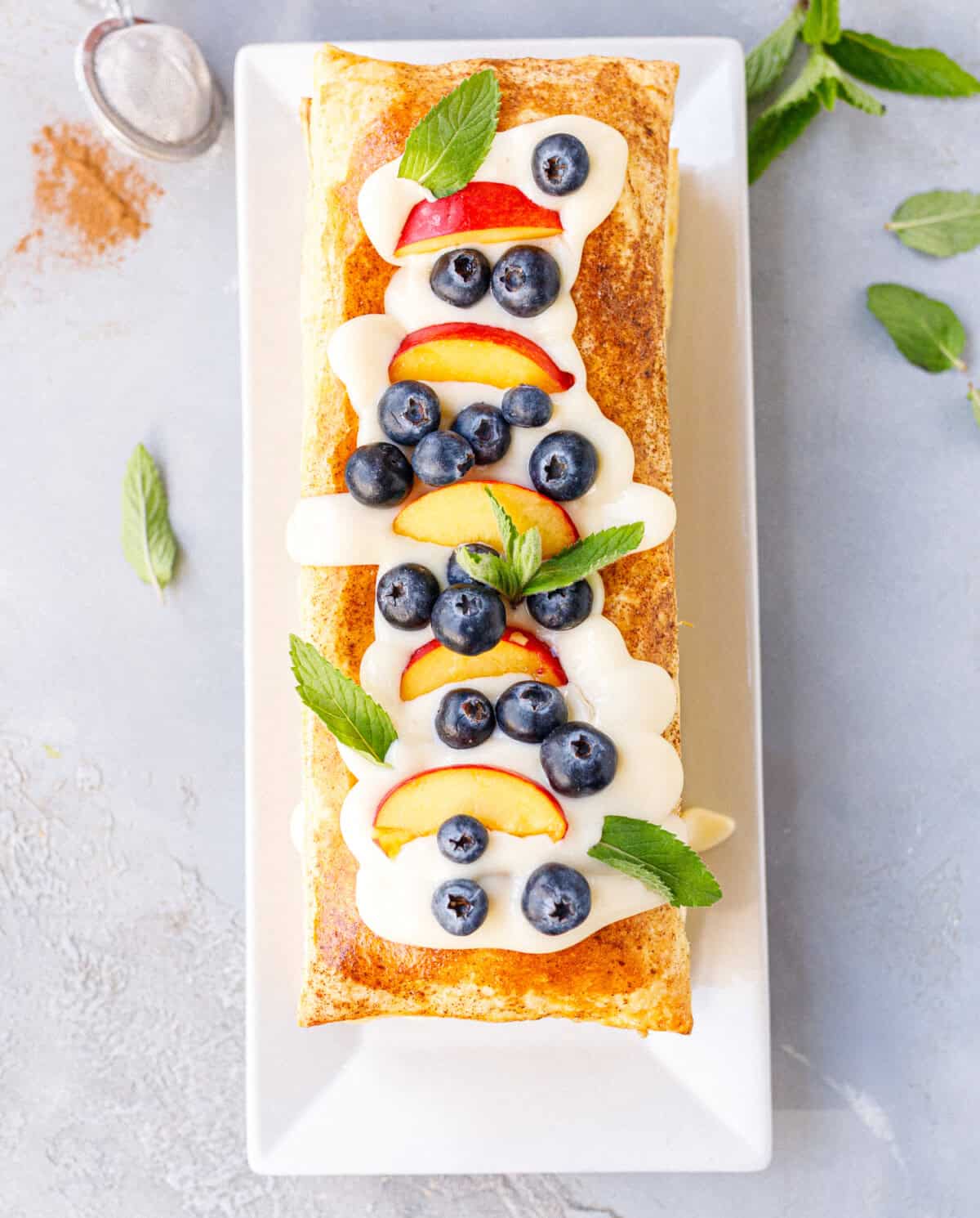 Angled view of a layered puff pastry tart dusted with powdered sugar, topped with vanilla cream, blueberries, nectarine slices, and mint leaves