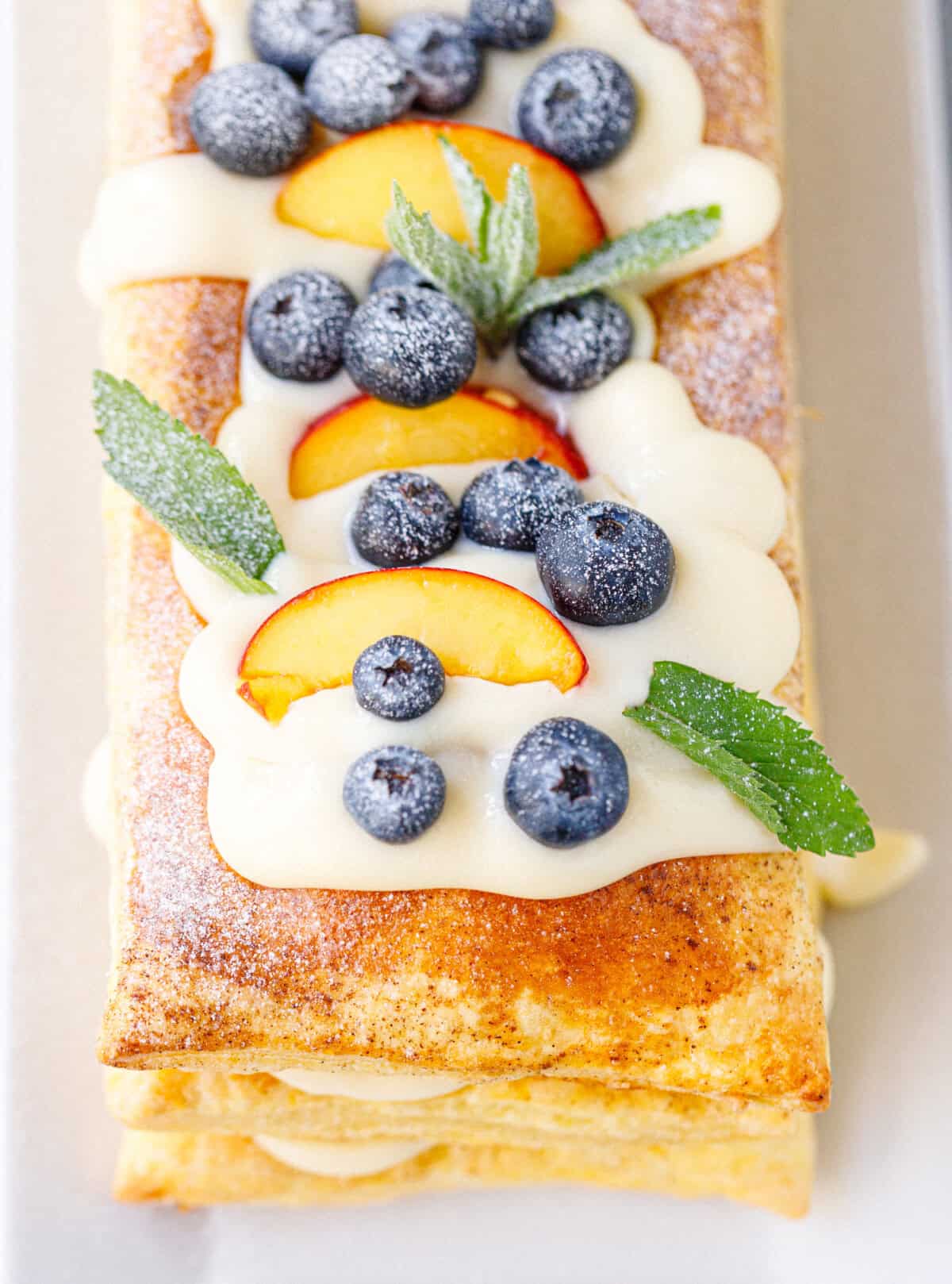 Close-up side view of a three-layer puff pastry tart showing the flaky pastry layers and vanilla cream filling between each layer