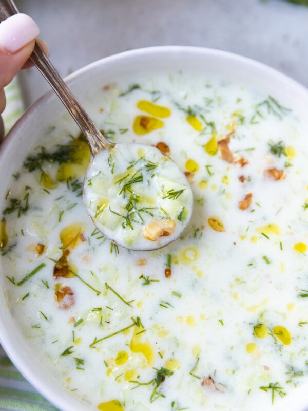 A bowl with cold cucumber soup and a soup spoon scooping out of it